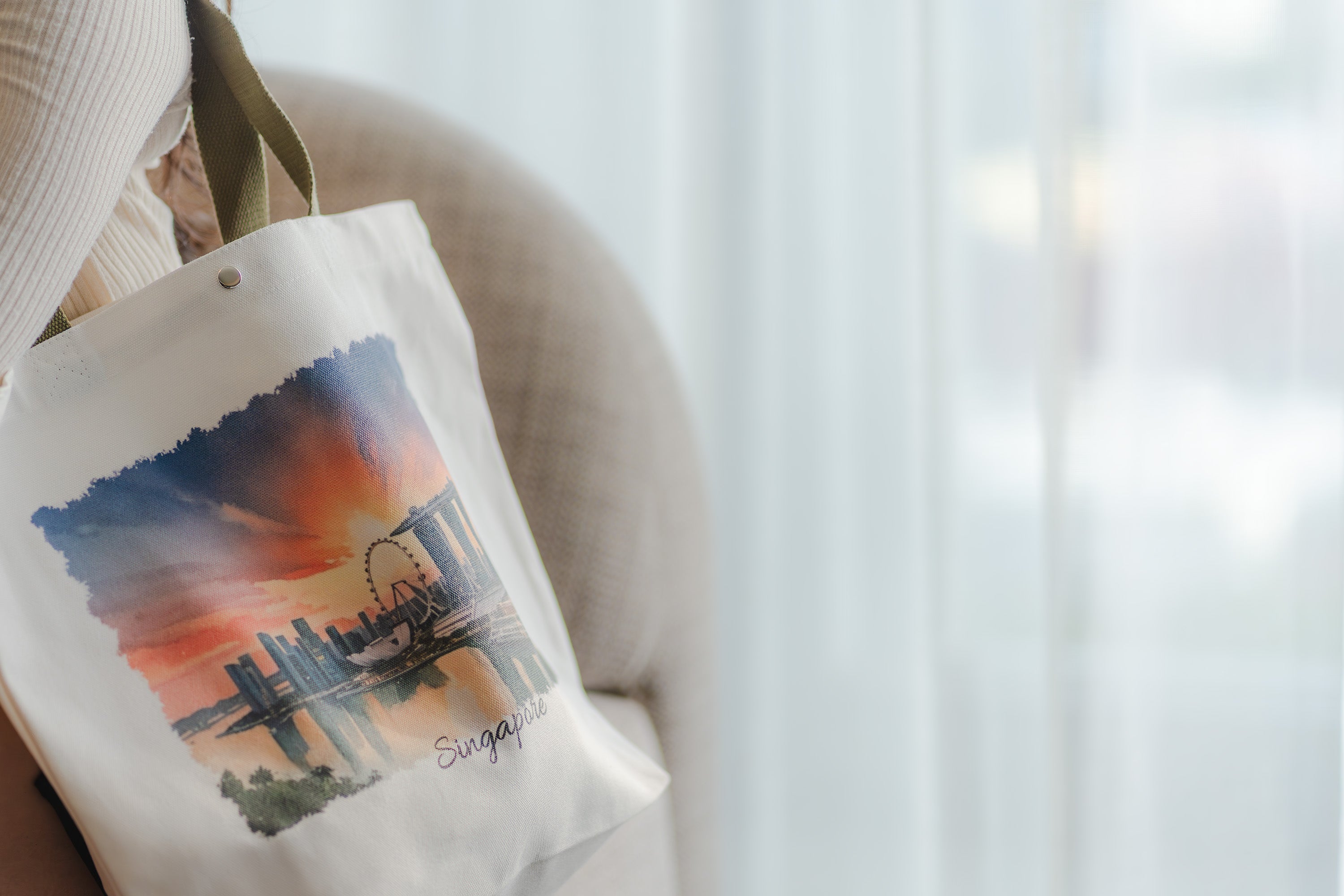 Tote bag with a scenic design and 'Singapore' text, hanging on a chair.