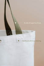 White tote bag with green straps on a beige background